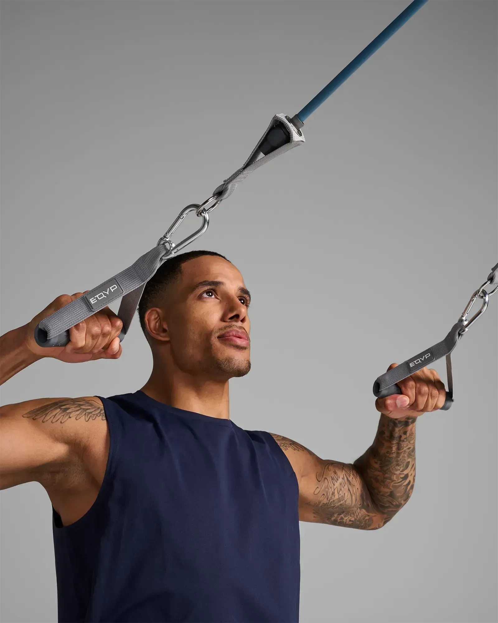 Man performing a standing bilateral lateral row using EQYP Power Tube 70 lbs blue resistance tube with gray handles and carabiner clips