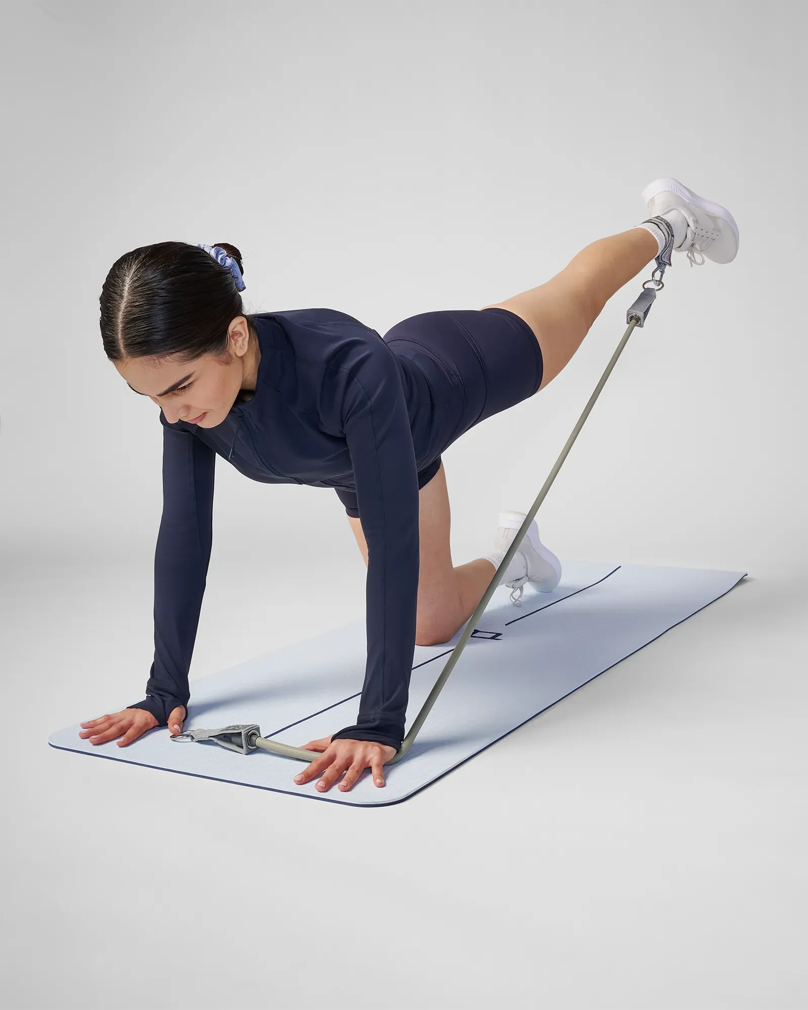 Woman performing a quadruped single-leg kickback with ankle strap on a yoga mat using EQYP Power Tube Extra Heavy gray resistance tube