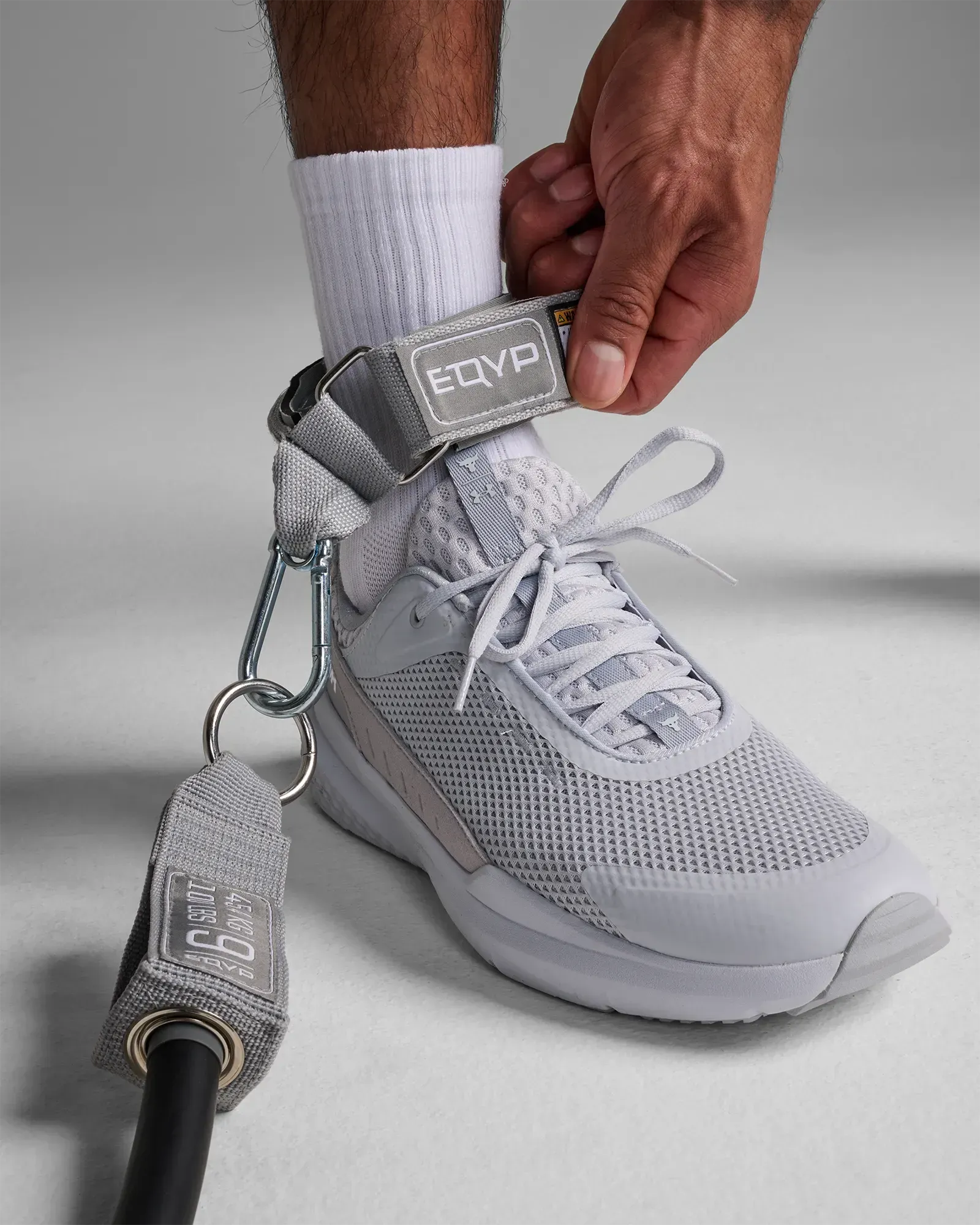 Man fastening the EQYP Power Tubes Ankle Strap around his ankle before a workout