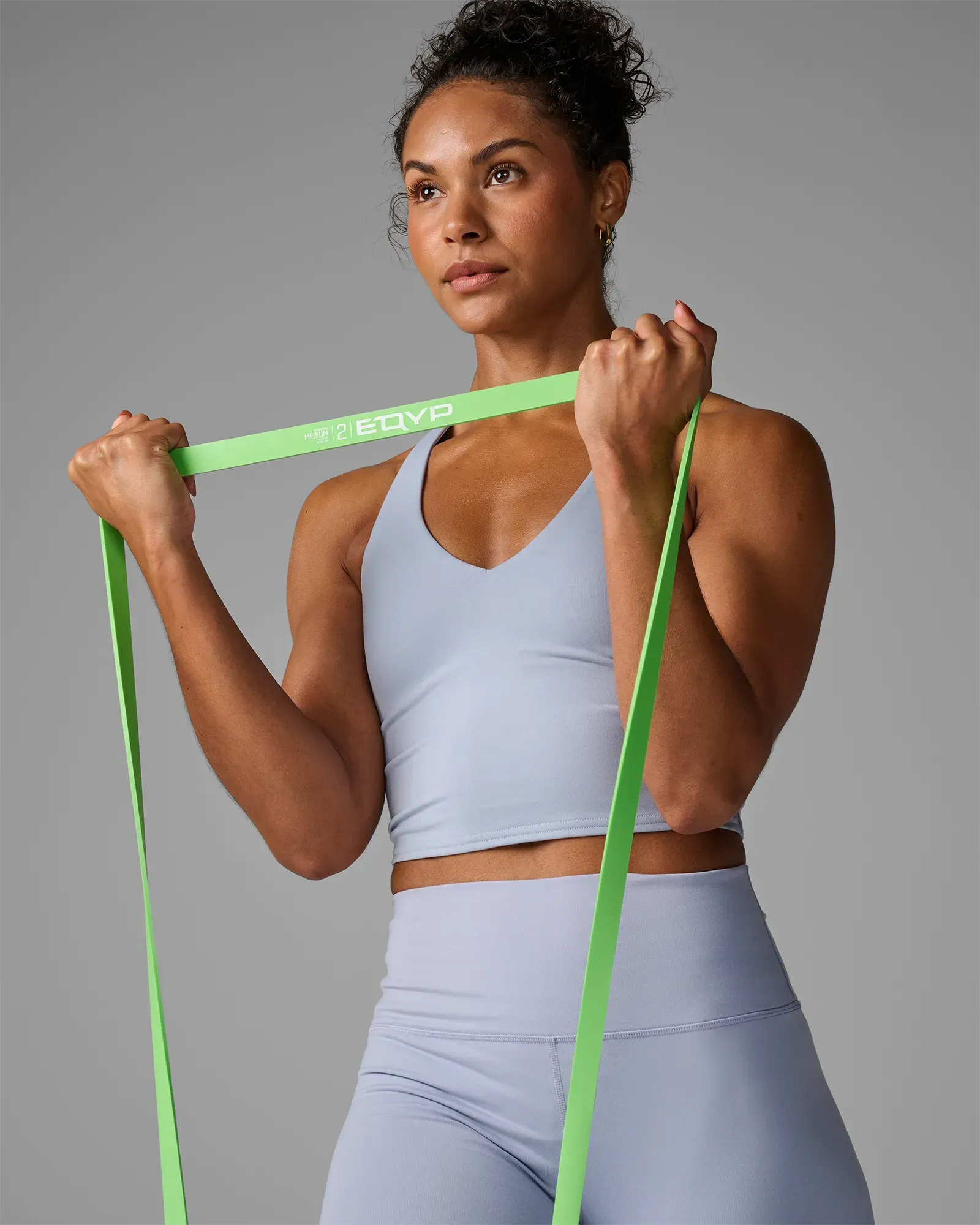 Woman performing a band pull-apart with EQYP green Super Band at chest height to strengthen rear deltoids and upper back