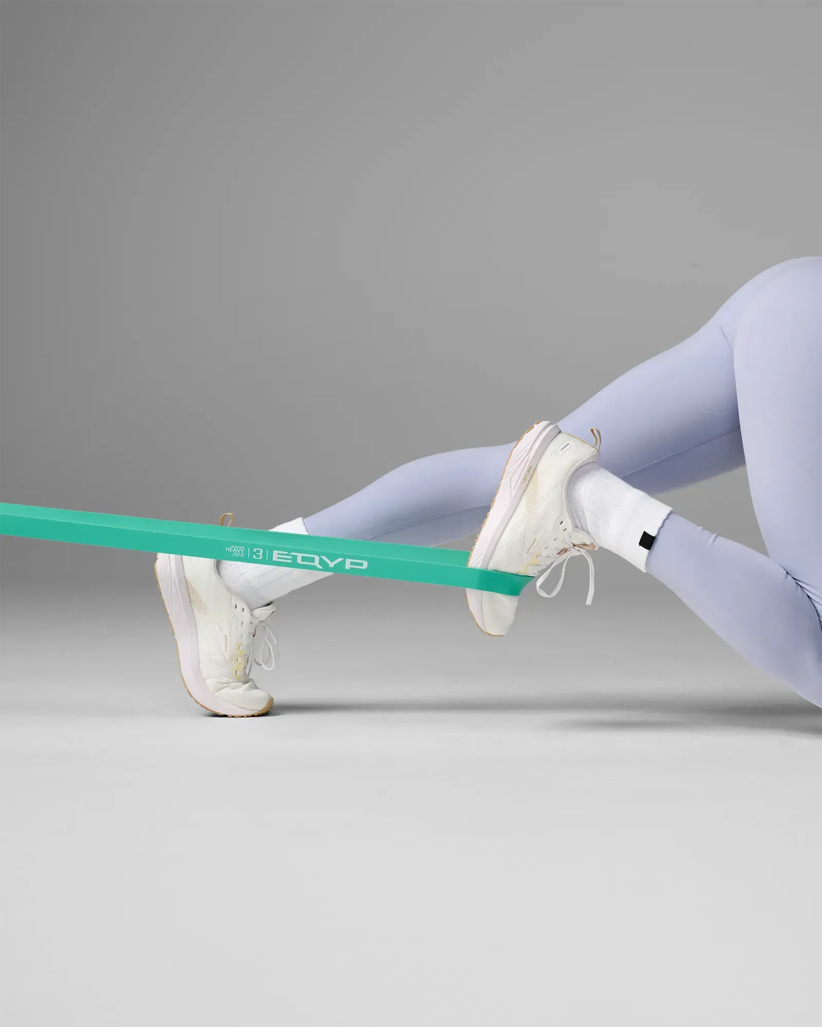 Woman performing leg exercise using an EQYP teal elastic wide super band around her foot