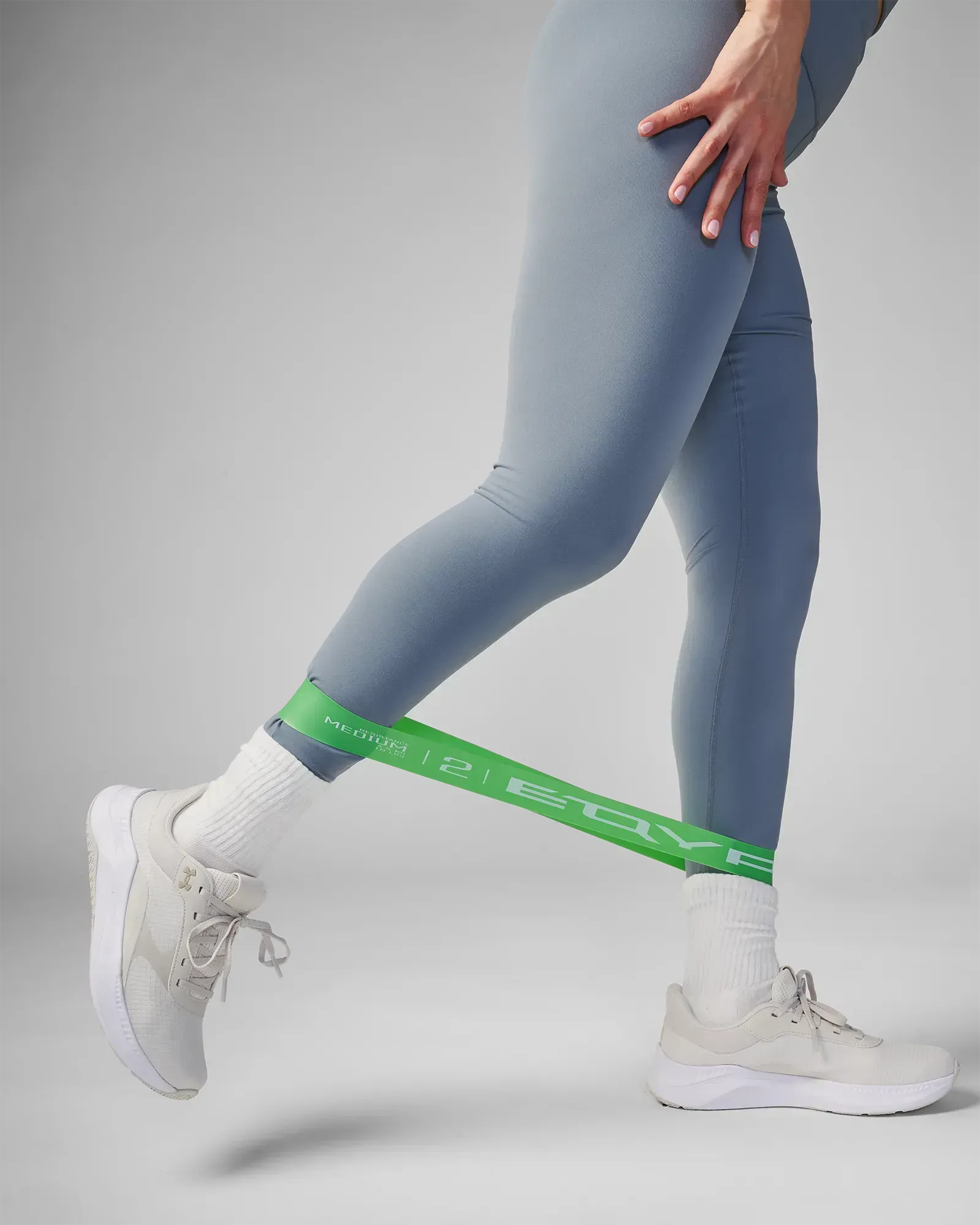 Woman performing a standing unilateral leg stretch using EQYP Power Loop Medium green resistance band around the ankles