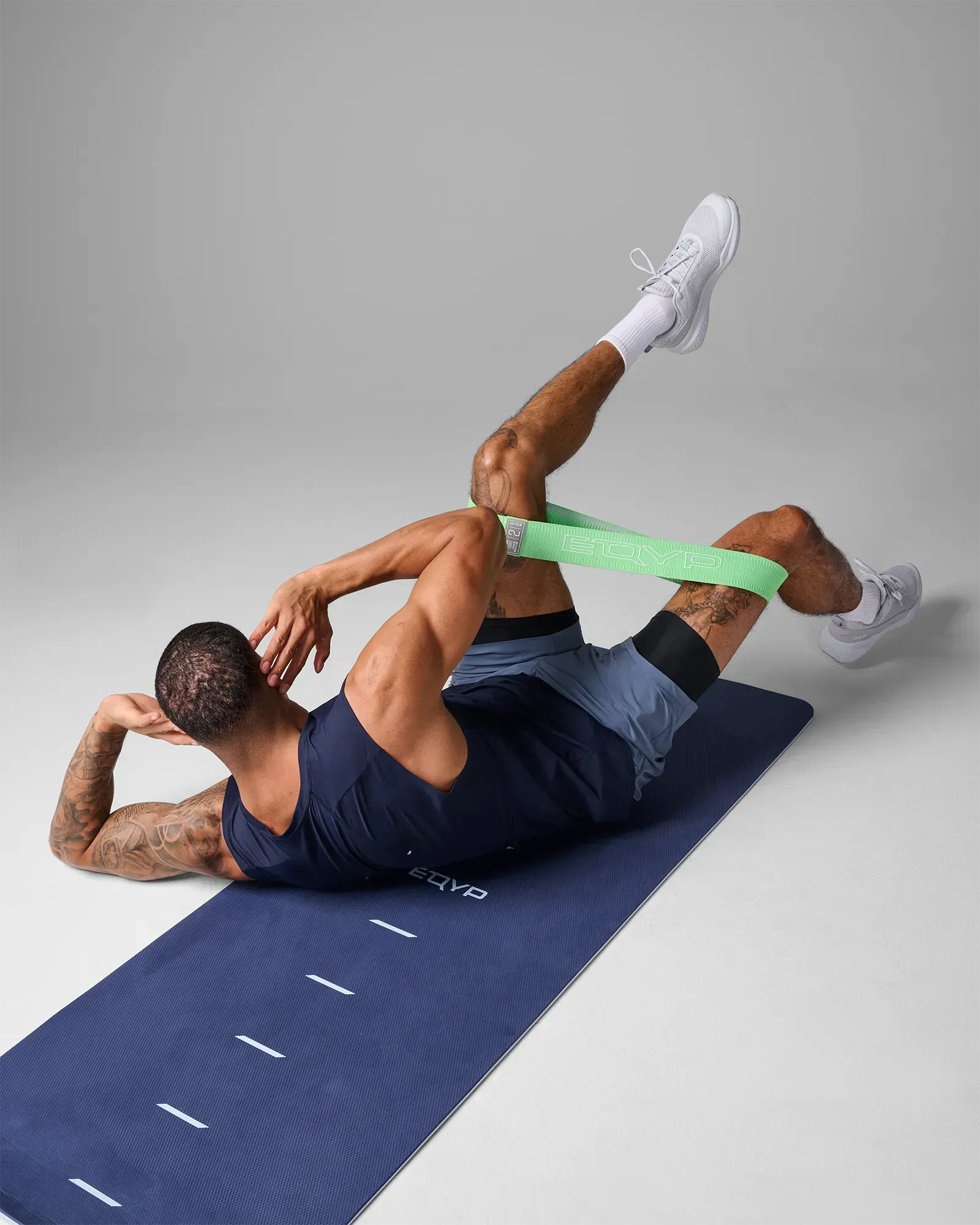 Man performing a supine glute bridge with leg extension on a yoga mat using an EQYP green elastic wide squat band around his thighs
