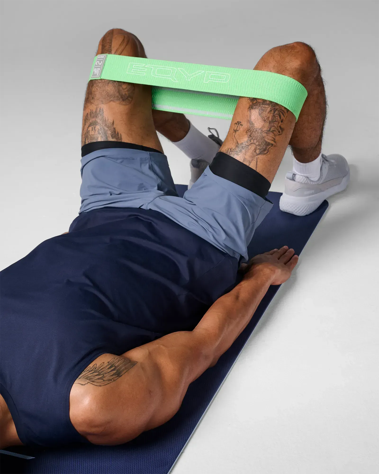 Man performing a supine glute bridge on a yoga mat using an EQYP green elastic wide squat band around his thighs