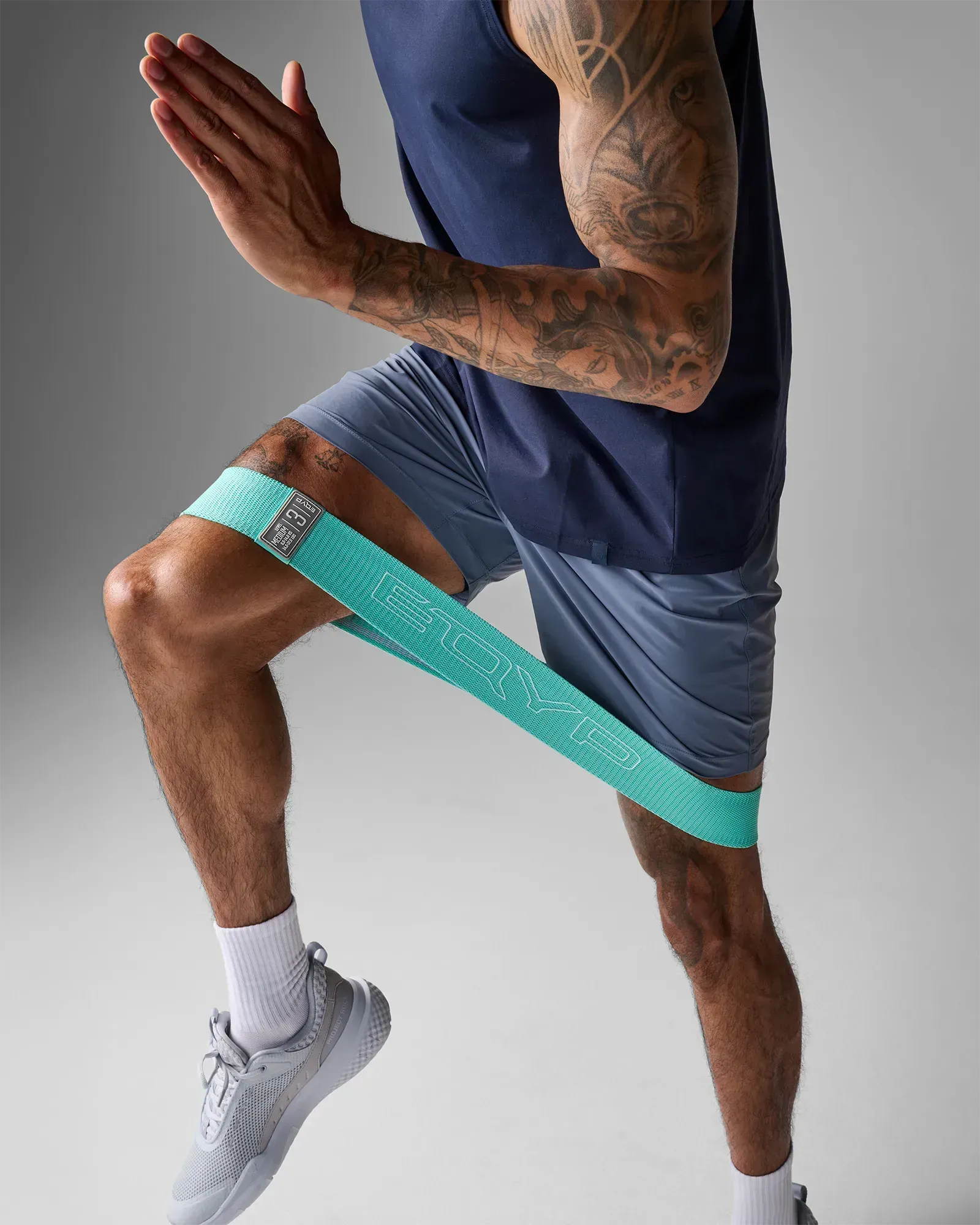 Man performing a standing knee drive using an EQYP teal elastic wide squat band around his thighs