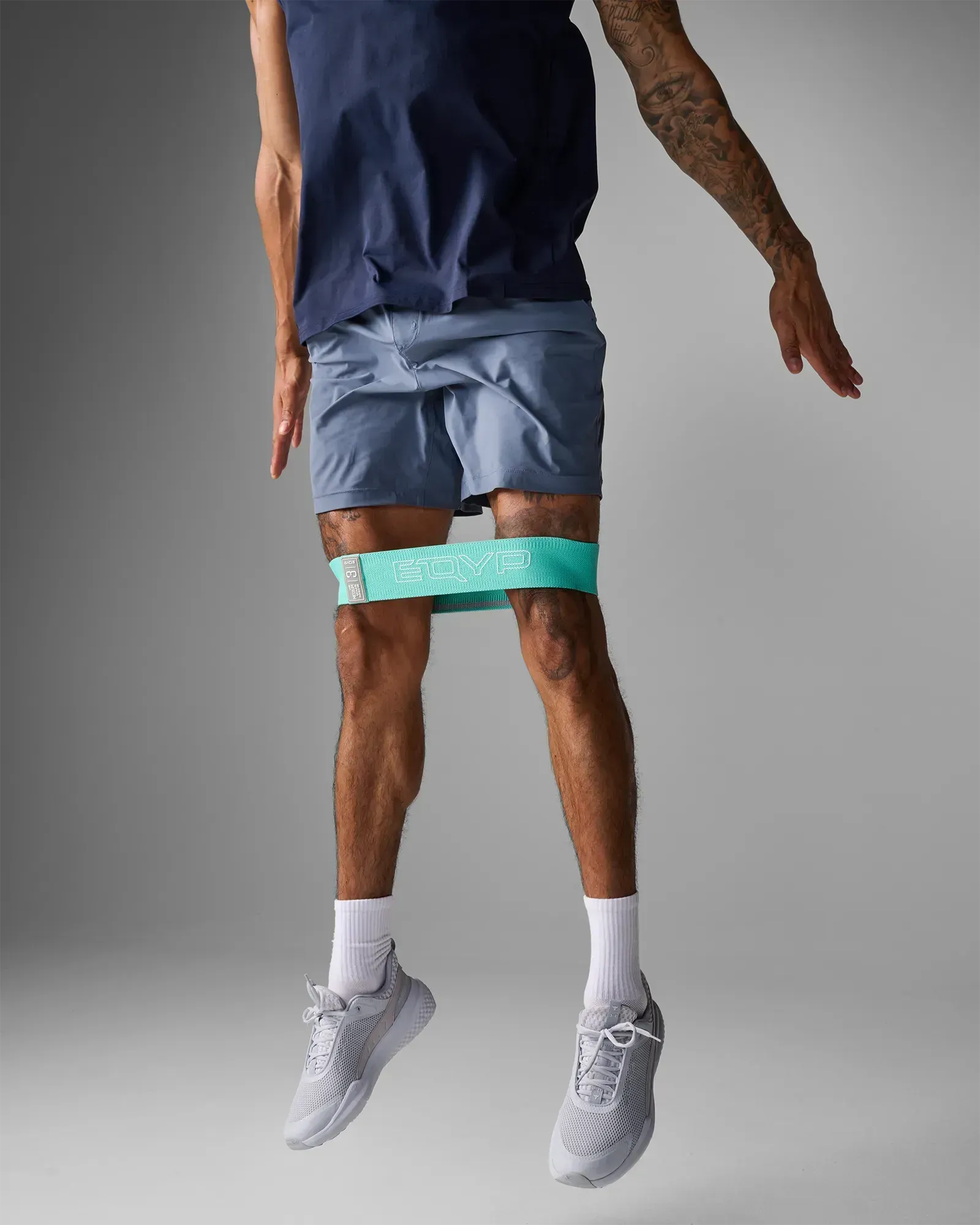 Man performing a lateral jump using an EQYP teal elastic wide squat band around his thighs