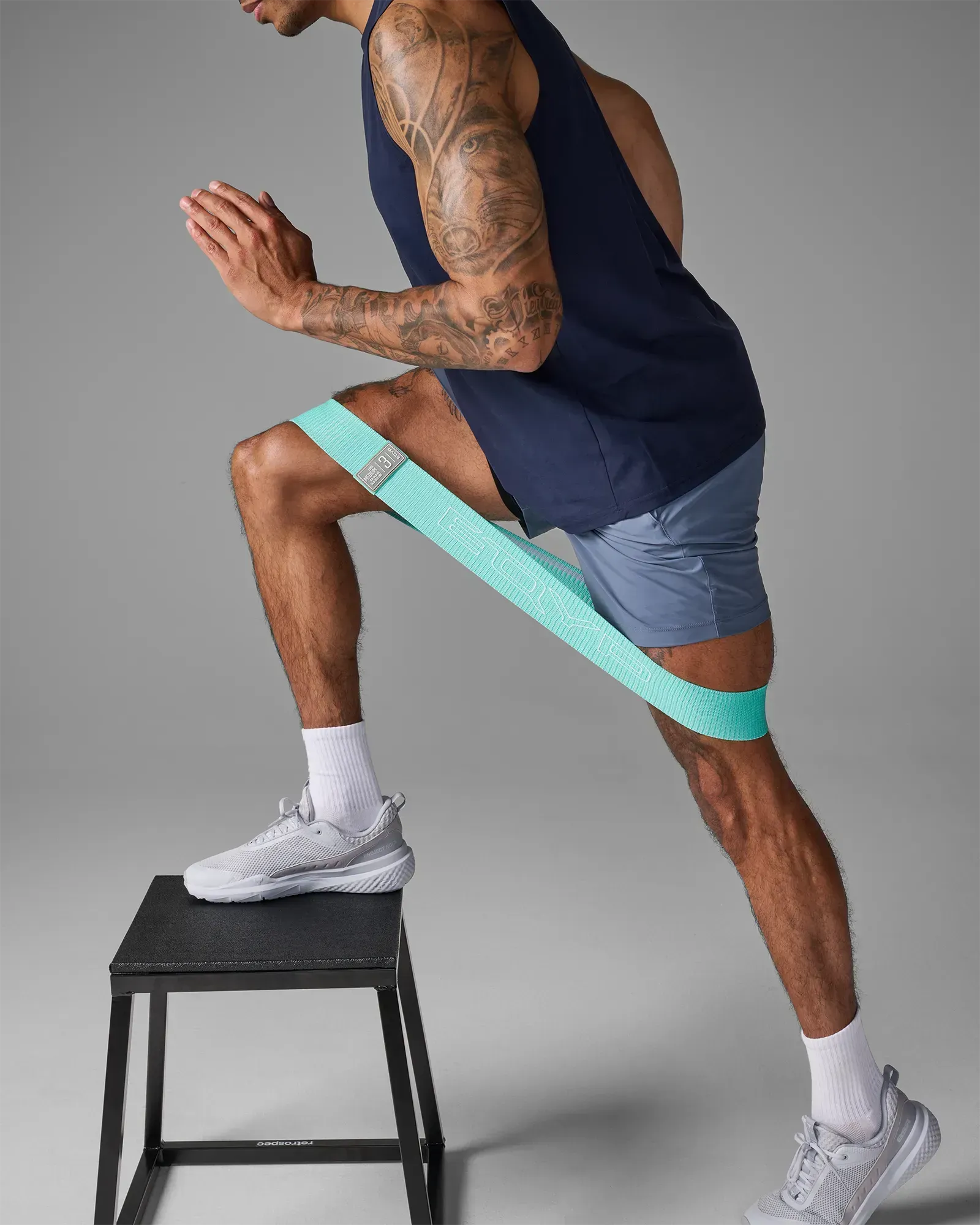 Man performing a step-up on a plyo step stool using an EQYP teal elastic wide squat band around his thighs