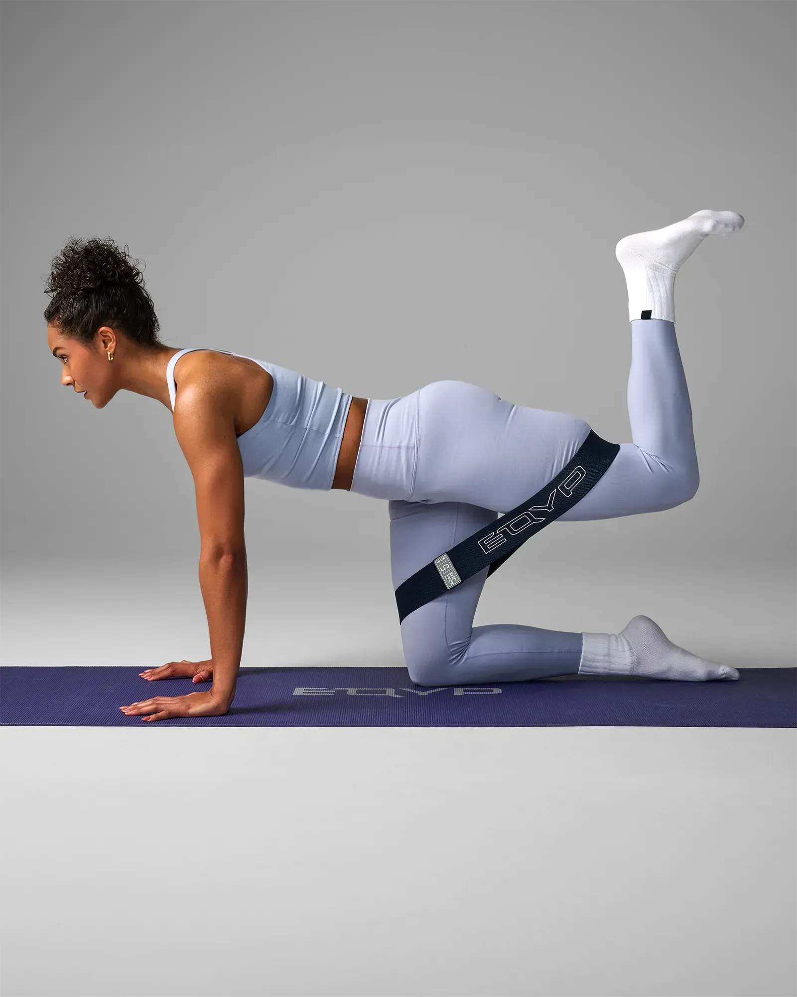 Woman performing a kneeling donkey kick on a yoga mat using an EQYP navy blue elastic wide squat band around her thighs