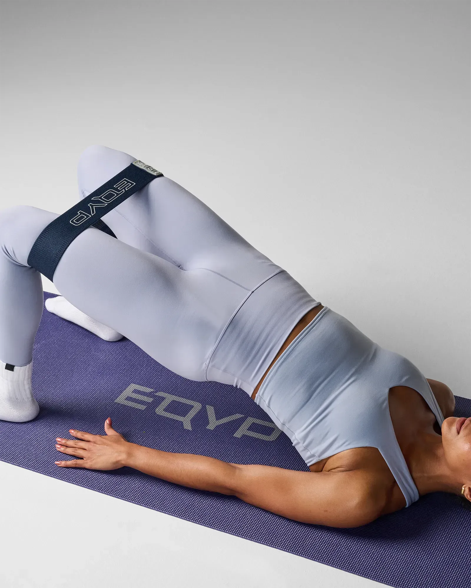 Woman performing a supine glute bridge on a yoga mat using EQYP navy blue elastic wide squat band around her thighs