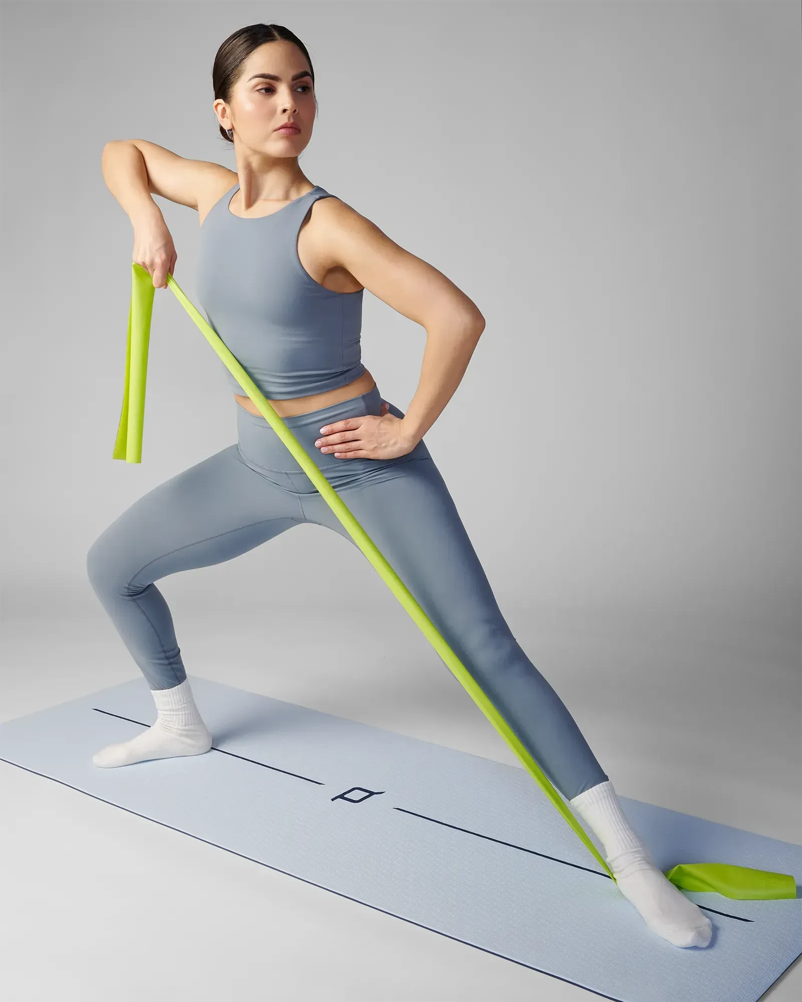 Woman performing a standing lateral lunge on a yoga mat using an EQYP green latex-free flat resistance band