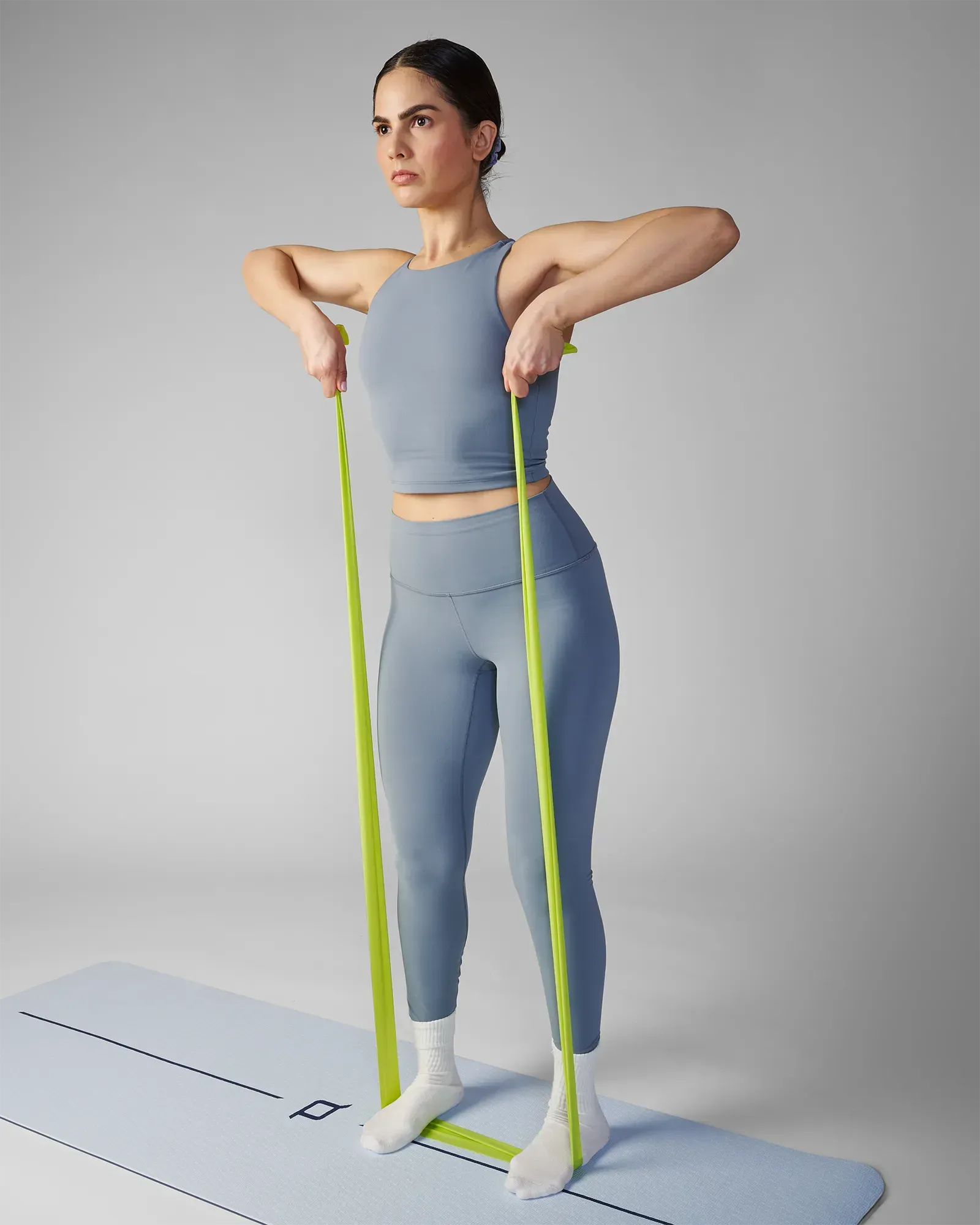 Woman performing a standing upright row on a yoga mat using an EQYP green latex-free flat resistance band