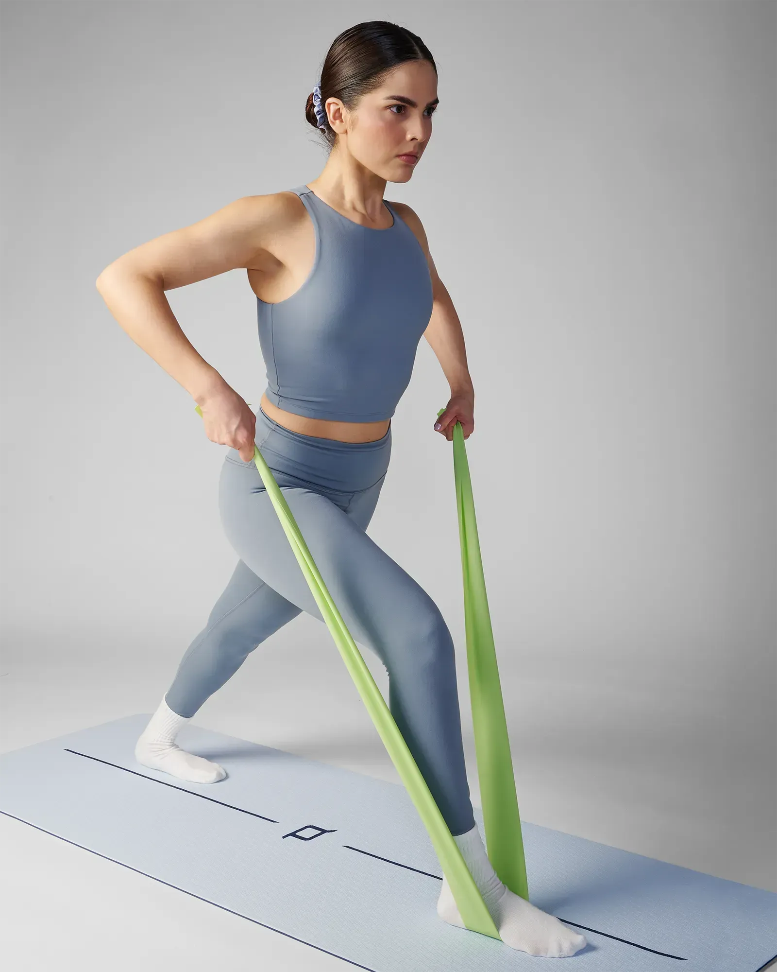 Woman performing a standing unilateral row on a yoga mat using an EQYP green flat resistance band