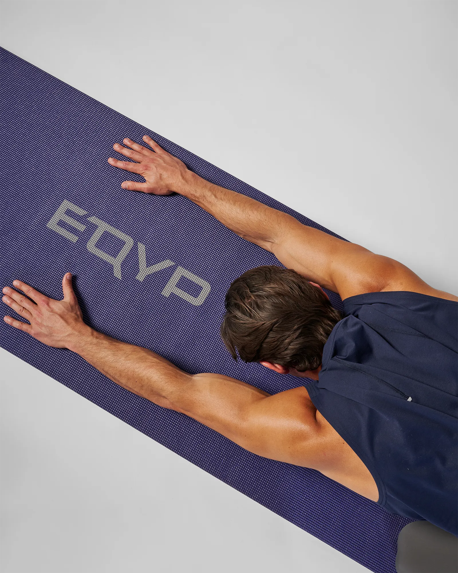 Man performing a child's pose stretch on an EQYP Yoga Mat in navy blue, overhead view showing the EQYP logo