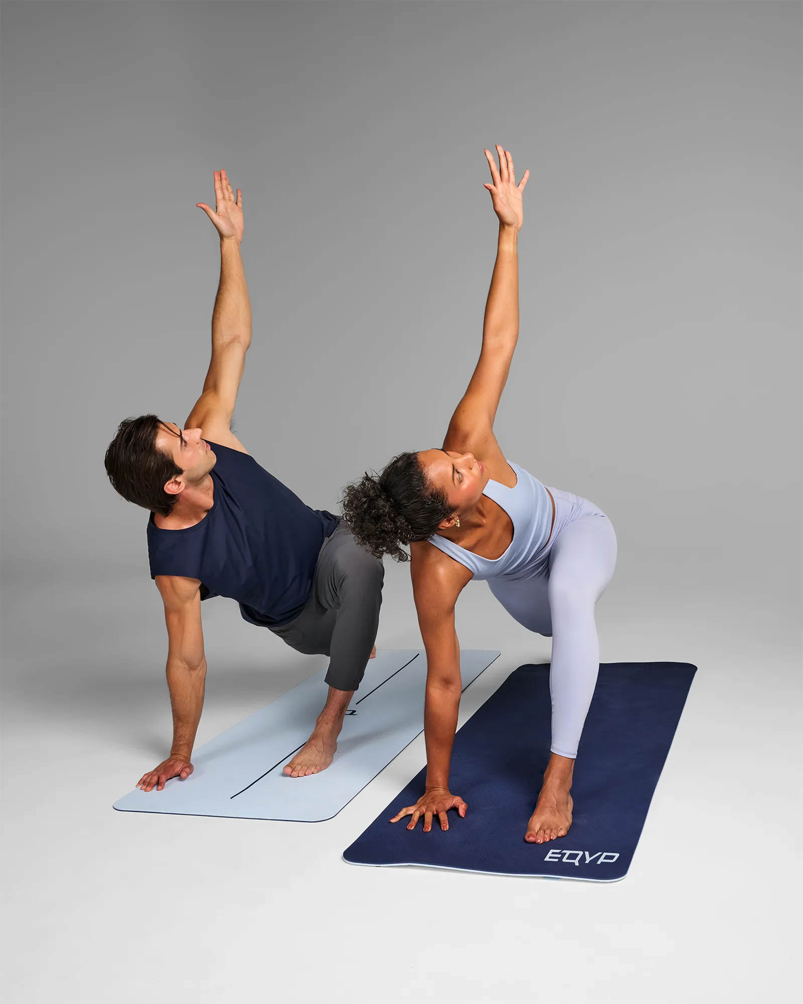 Man and woman performing a low lunge with arm extended up on two EQYP Dual Layer Yoga Mats