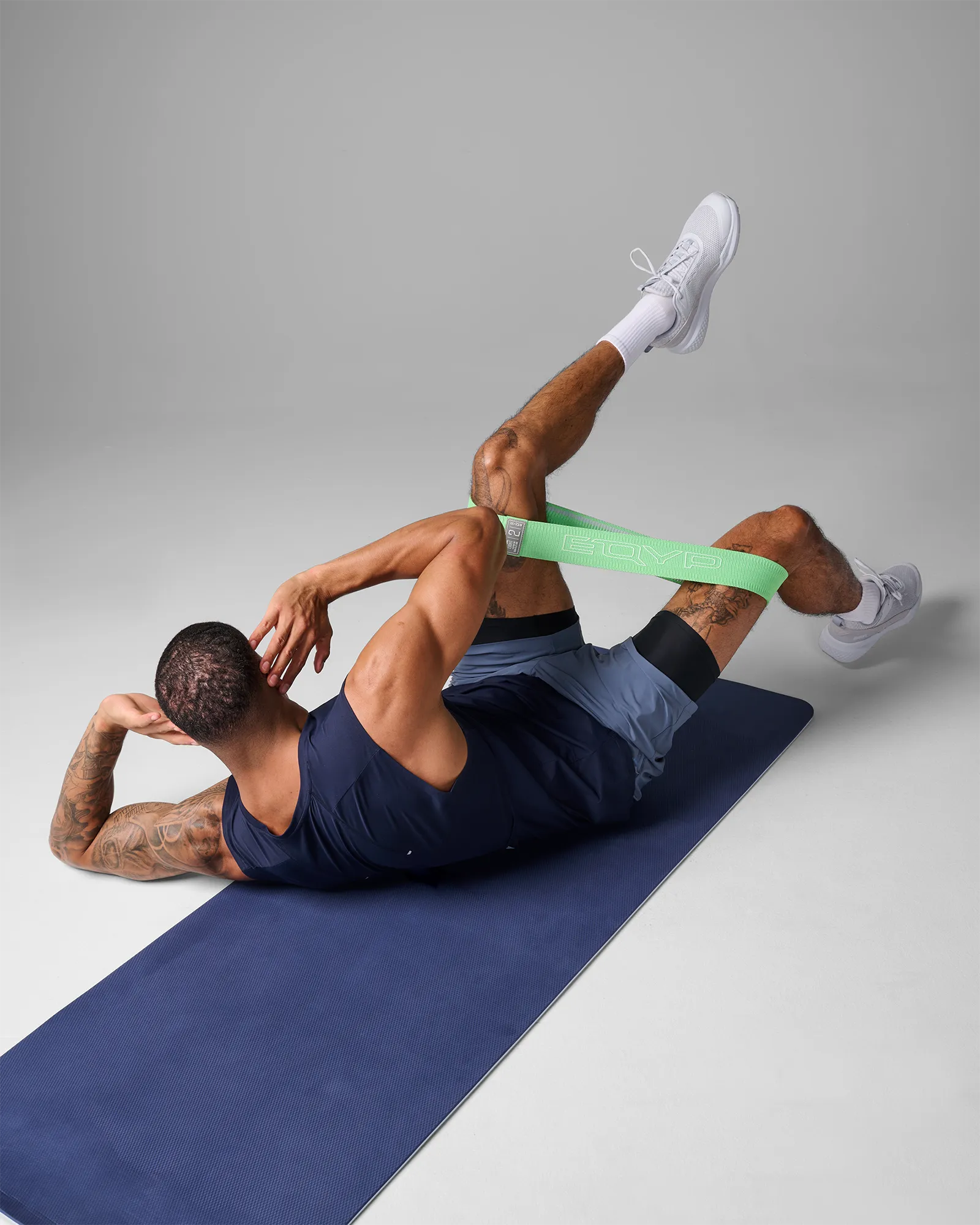 Man on EQYP Dual Layer Yoga Mat showing dark blue side performing bicycle crunches with band around thighs