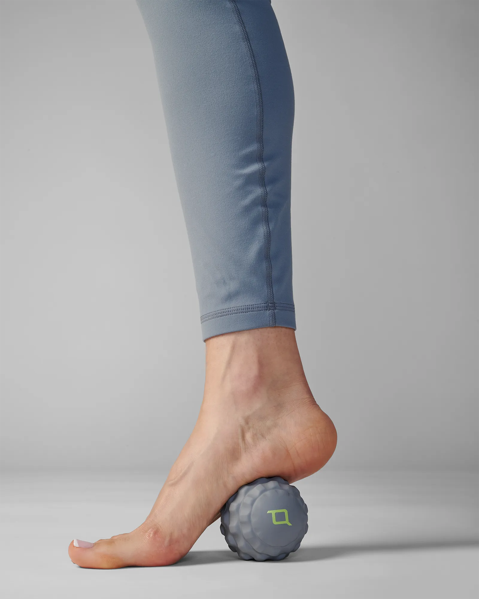 Person rolling small sized gray EQYP massage ball on back foot for muscle relief