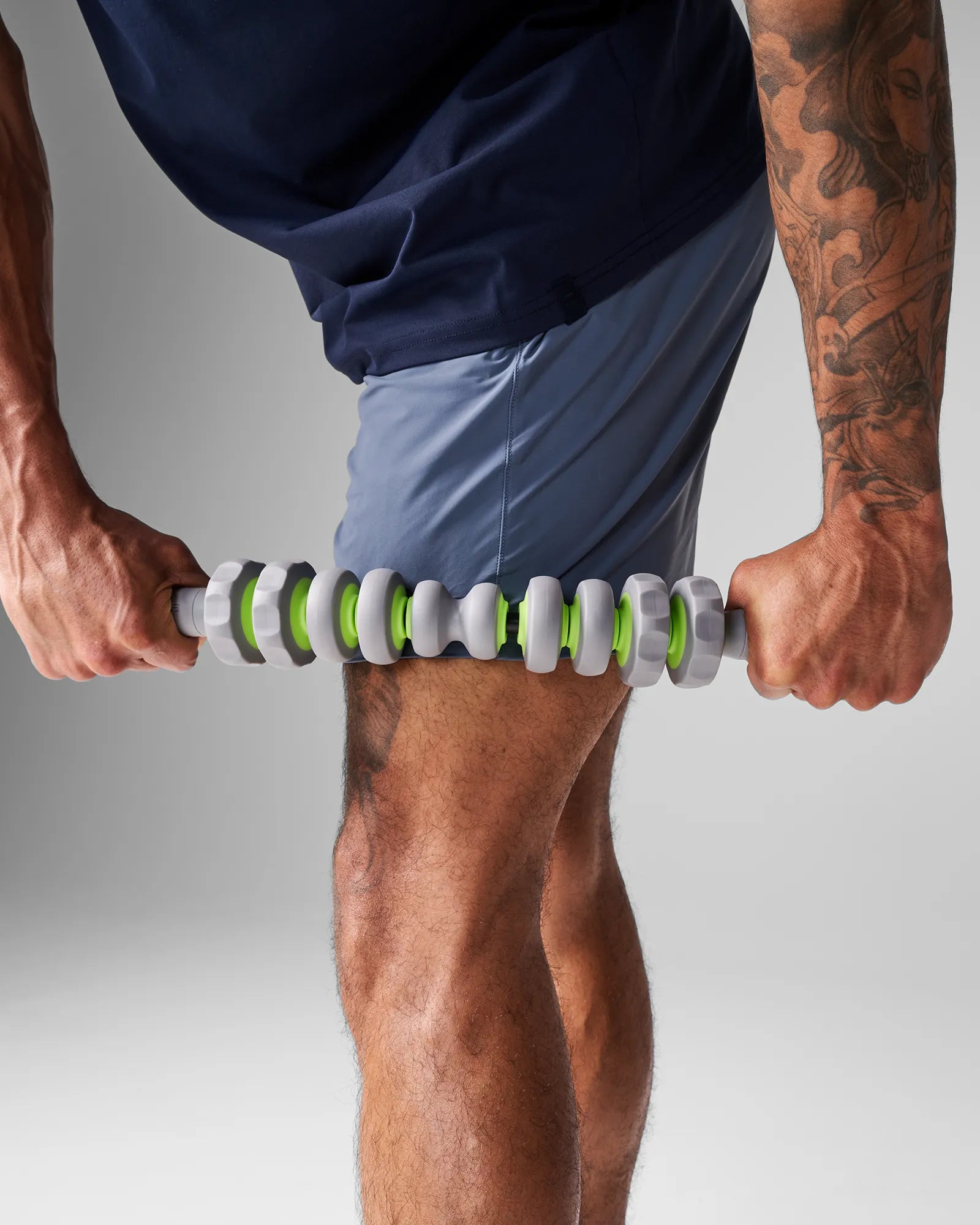 Man pressing EQYP 19 inch Massager Bar across upper quadricep to break up muscle knots and accelerate leg recovery