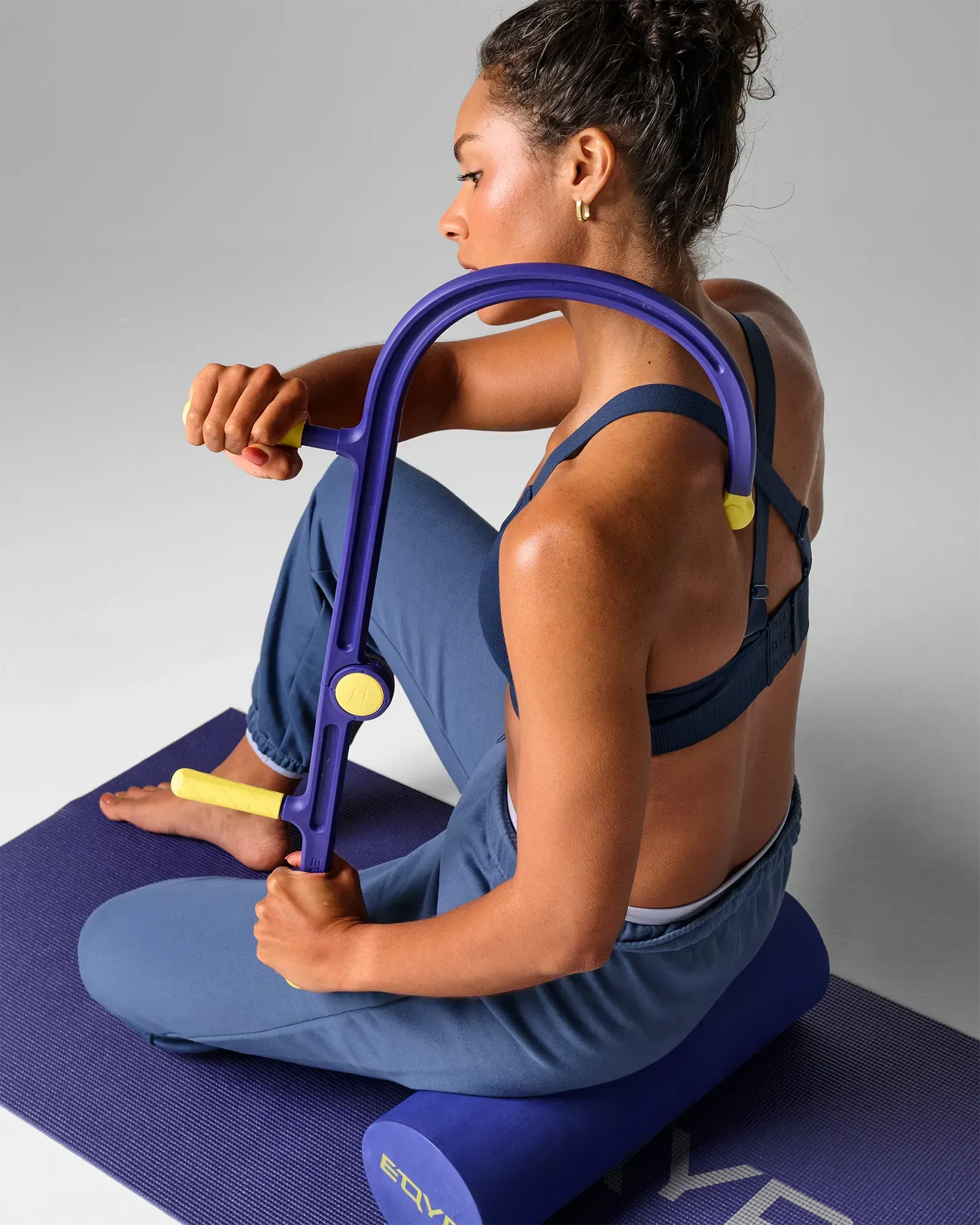 Woman on exercise mat using muscle hook recovery massager tool on upper back