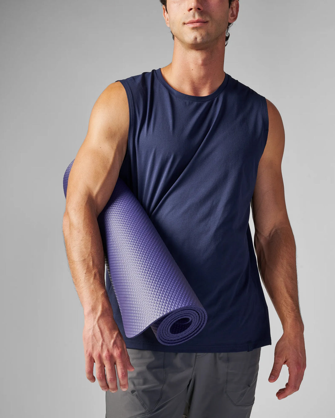 Man carrying a rolled EQYP Yoga Mat in navy blue under his arm showing the textured grip surface