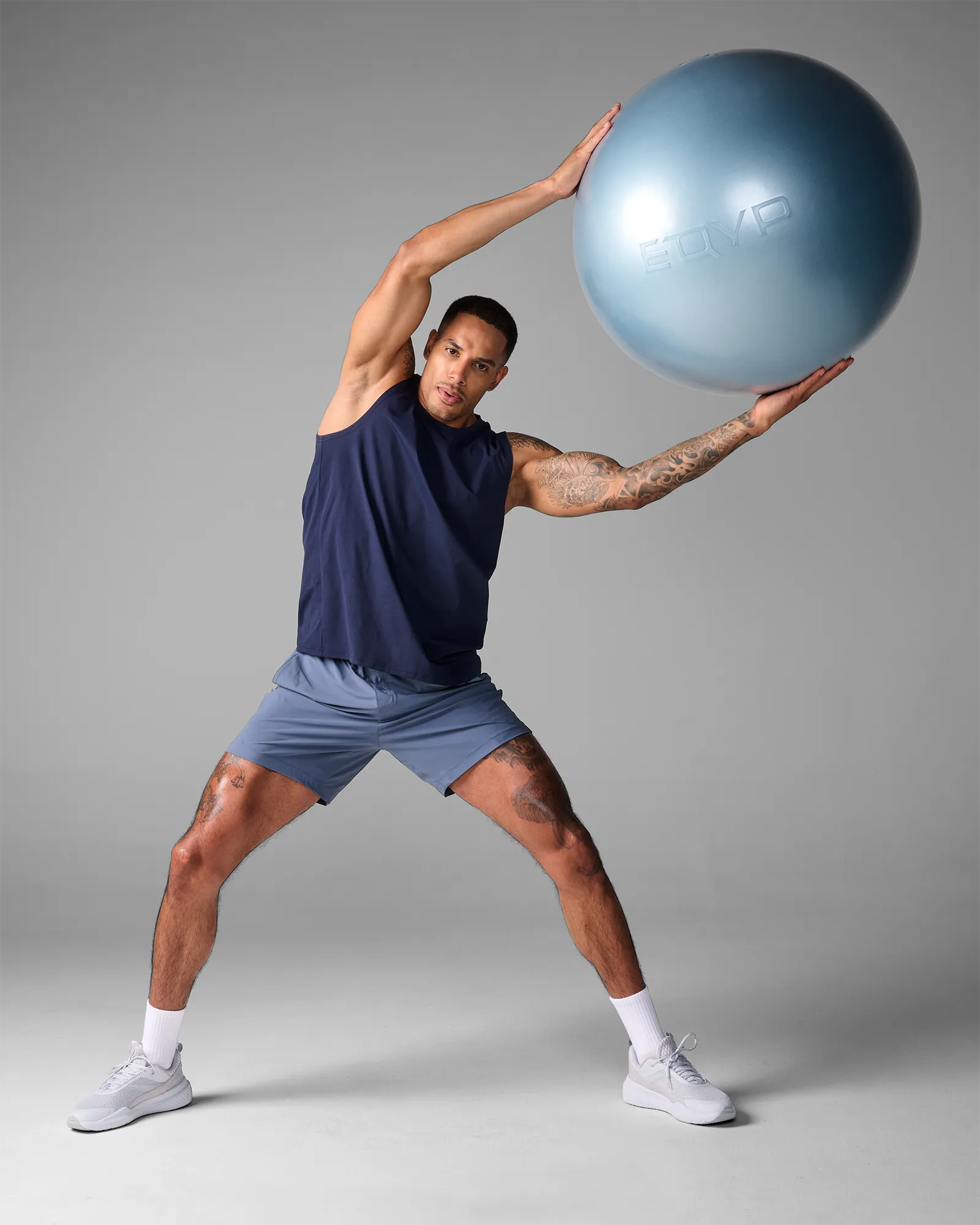 Man performing a standing unilateral lateral stretch holding an EQYP Pro Stability Ball 65cm overhead with a wide stance