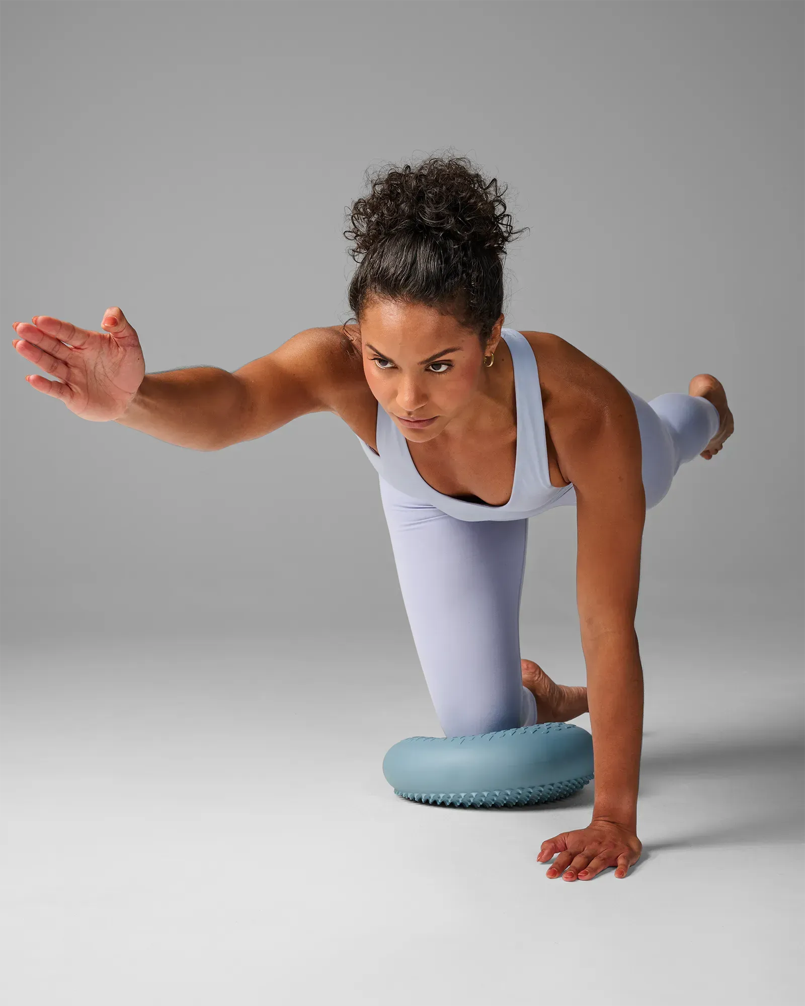 Woman performing a kneeling contralateral balance reach on EQYP Balance Disc with one arm extended forward, front-angle view