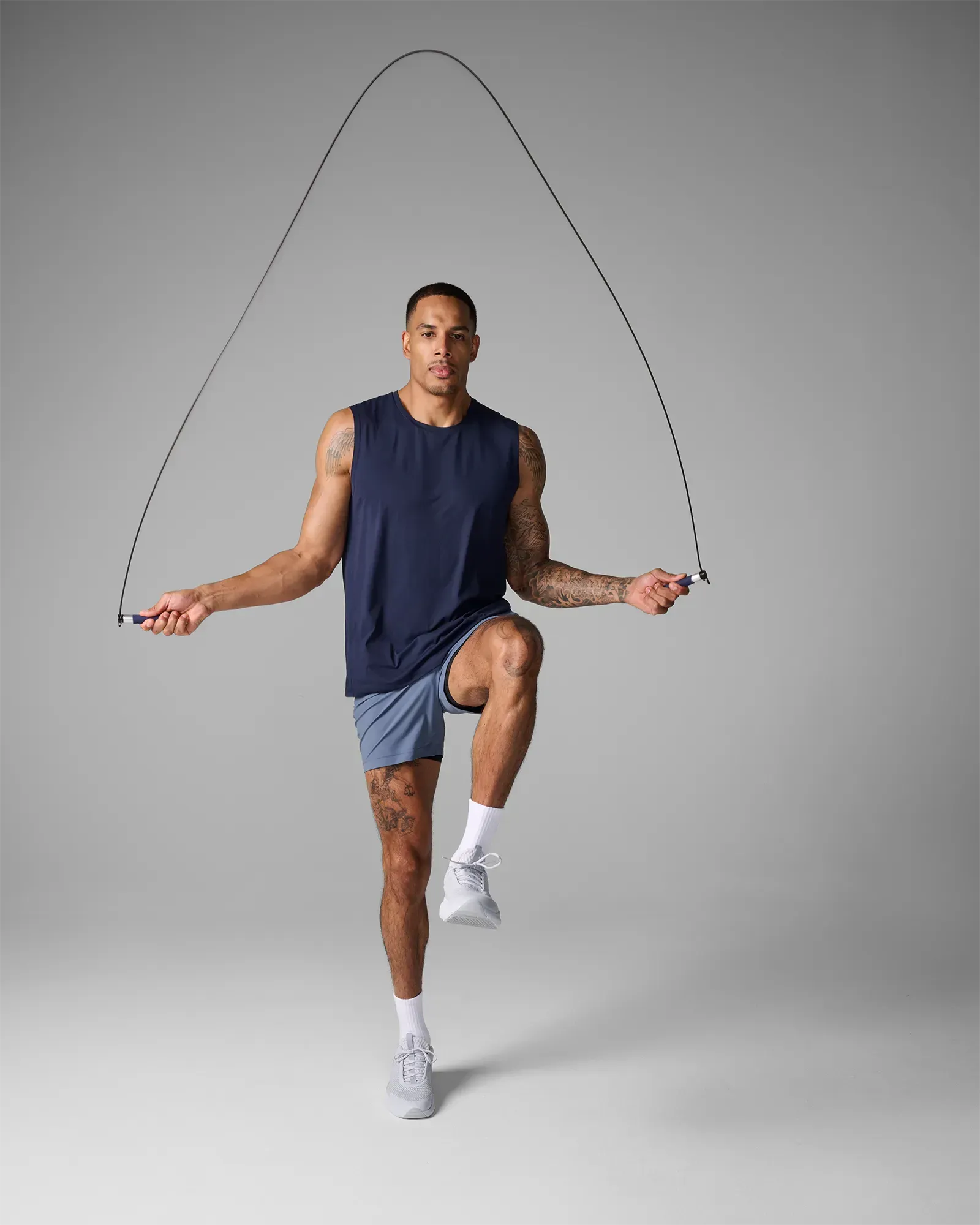 Man jumping rope with a high knee using EQYP Pro Cable Jump Rope with navy blue and aluminum handles and steel cable