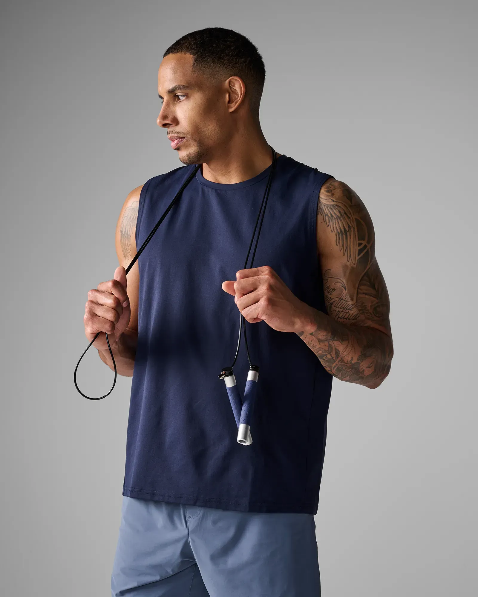 Man holding EQYP Pro Cable Jump Rope draped around his neck showing navy blue TPU grip handles and aluminum ends