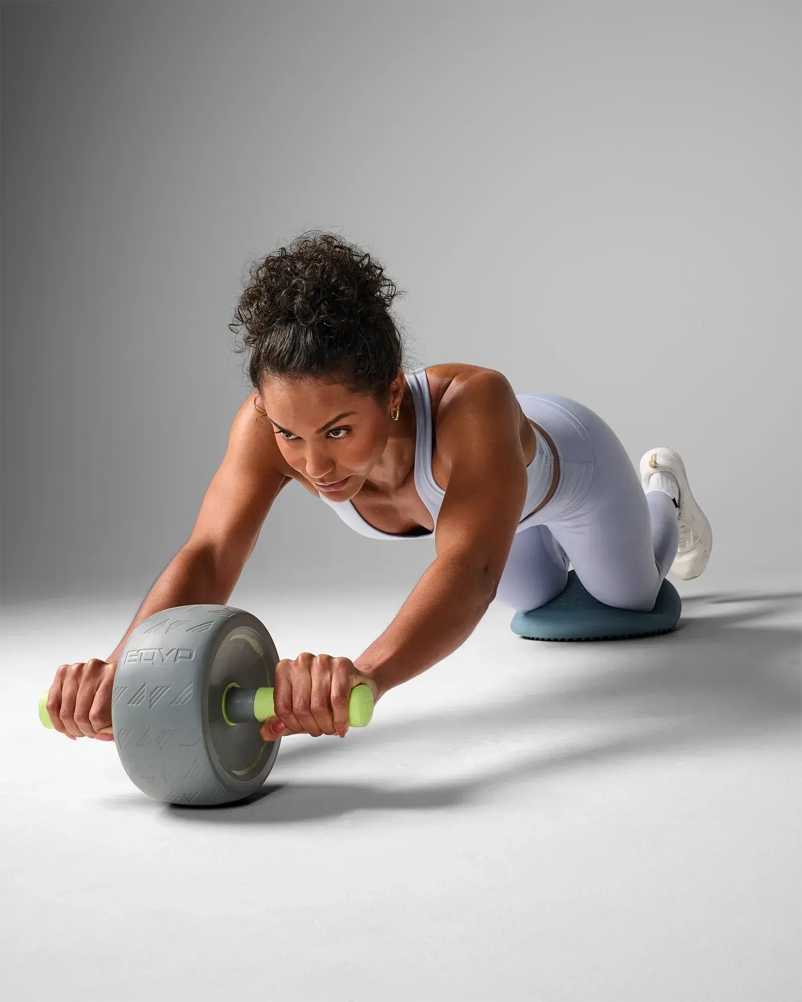 Woman performing a kneeling ab wheel rollout using the EQYP Q-Tech Ab Wheel with gray wheel and neon green handles with balance disc