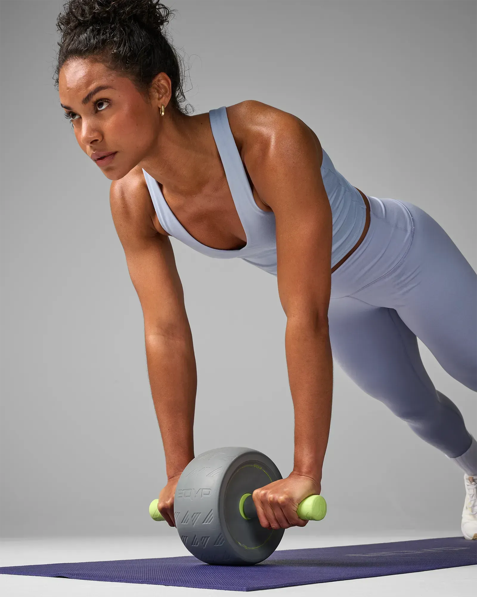 Woman performing a plank ab wheel rollout on a yoga mat using the EQYP Q-Tech Ab Wheel with gray wheel and neon green handles